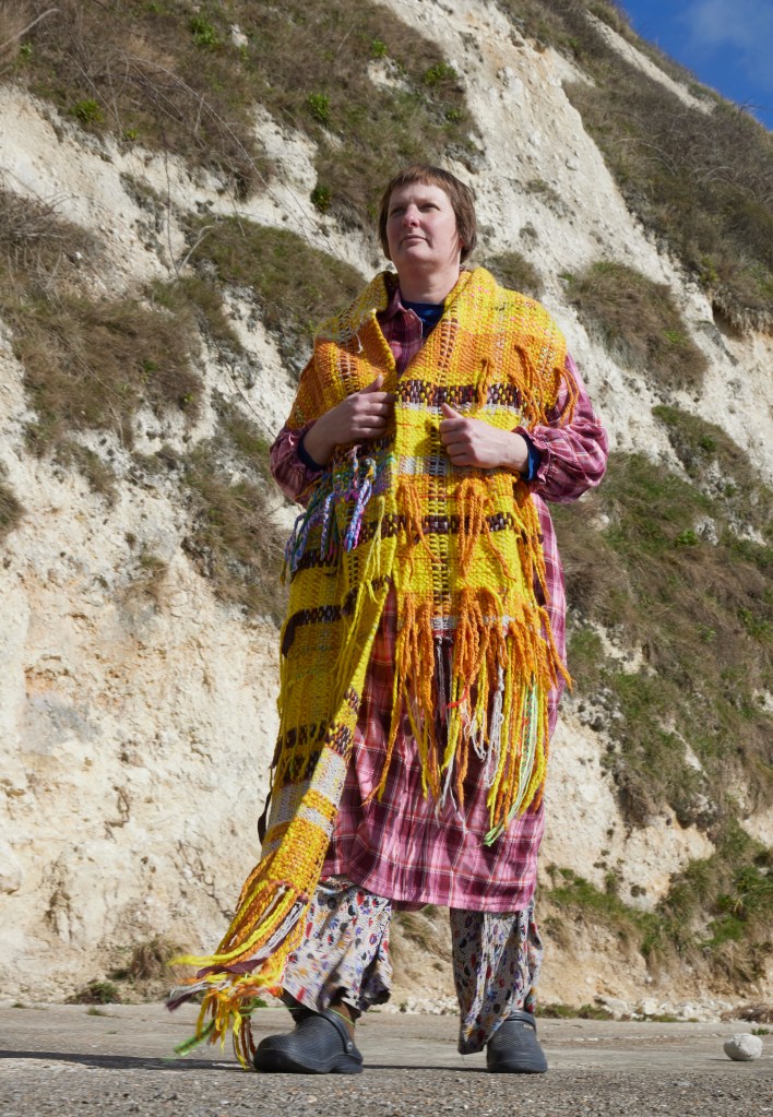 Nikki Tompsett standing by cliff at Warren Beach, Folkestone, wearing a dramatic textured woven scarf by Dawson Road studio